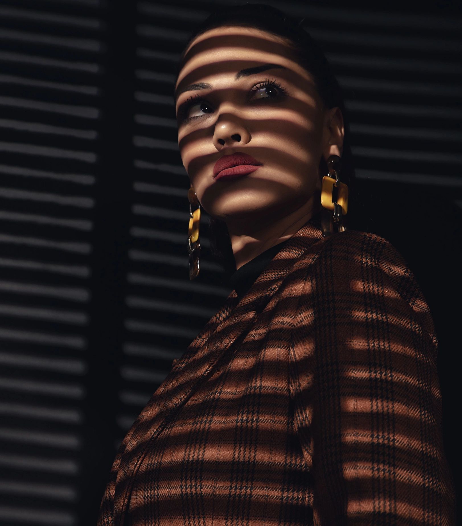 Side view of beautiful young woman in shade of jalousie.