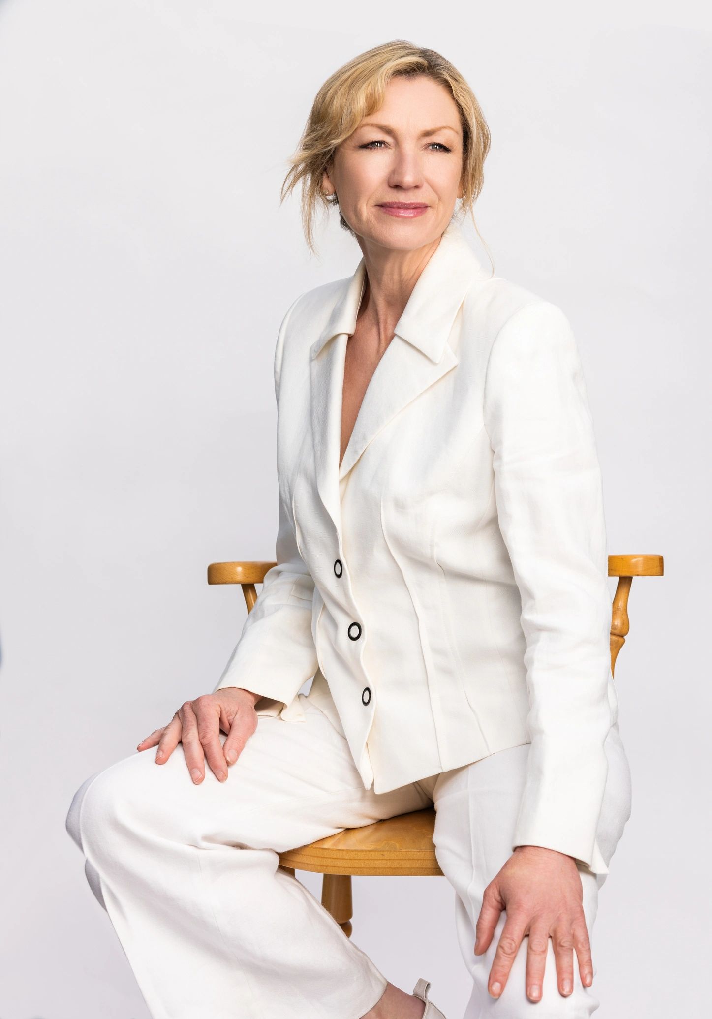Elegant middle-aged woman in a white suit seated on a stool